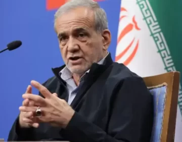 ایرانی صدر مسعود پزشکیان ڈائس پر لگے مائیکروفونز کے سامنے بیٹھے ہوئے گفتگو کر رہے ہیں اور اپنے دونوں ہاتھوں کی انگلیاں آپس میں ملائے اشارہ کر رہے ہیں