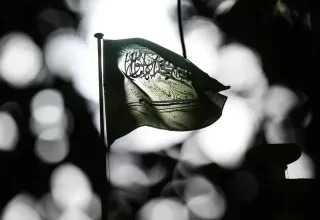 تاریک اور دھیمے پس منظر میں روشن بِلور (Bokeh) اثرات کے سامنے ہوا میں لہراتا ہوا سعودی عرب کا قومی پرچم