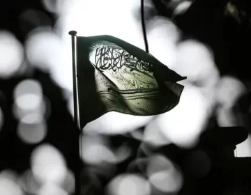 تاریک اور دھیمے پس منظر میں روشن بِلور (Bokeh) اثرات کے سامنے ہوا میں لہراتا ہوا سعودی عرب کا قومی پرچم