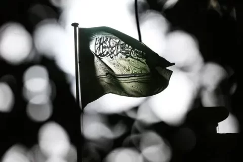 تاریک اور دھیمے پس منظر میں روشن بِلور (Bokeh) اثرات کے سامنے ہوا میں لہراتا ہوا سعودی عرب کا قومی پرچم