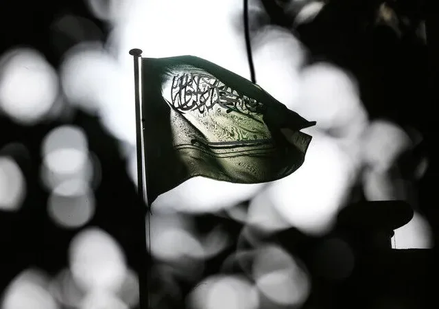 تاریک اور دھیمے پس منظر میں روشن بِلور (Bokeh) اثرات کے سامنے ہوا میں لہراتا ہوا سعودی عرب کا قومی پرچم